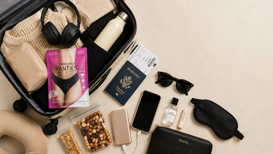 Carry-on travel essentials packed for a long flight including passport, headphones, charger, snacks, and Panty Fresh® On-The-Go Underwear Kit.